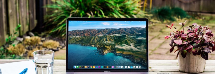 macbook pro beside clear drinking glass on brown wooden table
